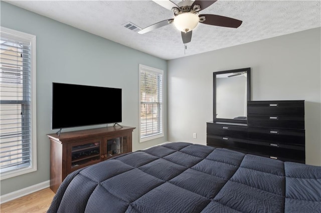 bedroom featuring visible vents, ceiling fan, baseboards, wood finished floors, and a textured ceiling