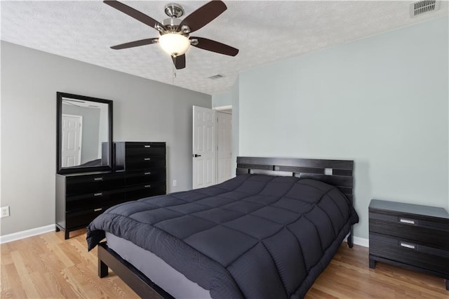 bedroom with visible vents, a textured ceiling, baseboards, and wood finished floors