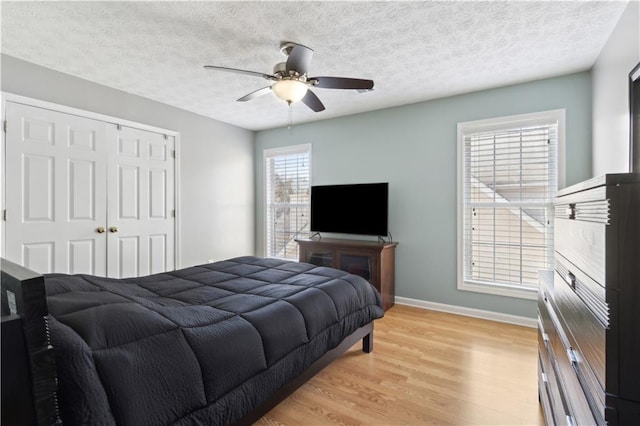 bedroom with a closet, baseboards, light wood finished floors, and a textured ceiling