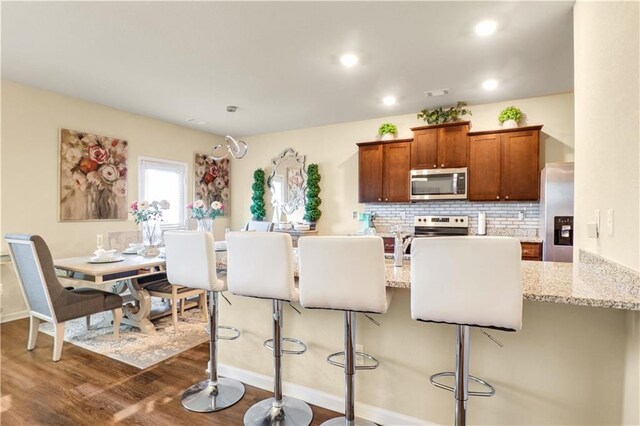 kitchen with decorative backsplash, appliances with stainless steel finishes, light stone counters, and a kitchen breakfast bar