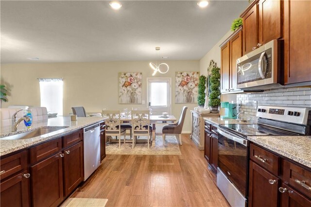 kitchen featuring light stone counters, sink, decorative light fixtures, and appliances with stainless steel finishes