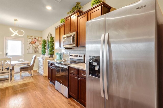 kitchen with light stone counters, light hardwood / wood-style flooring, backsplash, decorative light fixtures, and appliances with stainless steel finishes