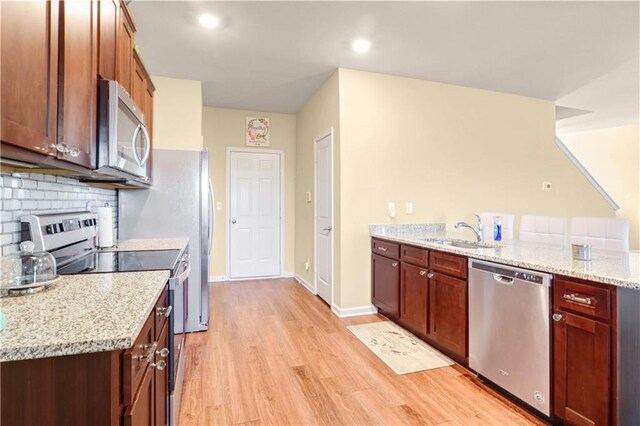 kitchen with light stone countertops, sink, light hardwood / wood-style floors, decorative backsplash, and appliances with stainless steel finishes