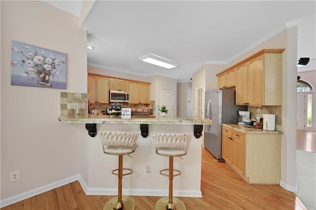 kitchen featuring light wood-type flooring, stainless steel appliances, light brown cabinets, kitchen peninsula, and a kitchen breakfast bar