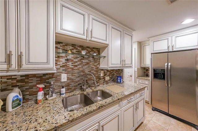 kitchen with sink, stainless steel refrigerator with ice dispenser, light stone countertops, tasteful backsplash, and white cabinetry