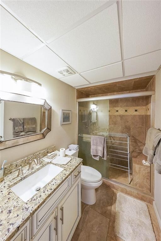 bathroom with tile patterned flooring, vanity, toilet, and a shower with shower door