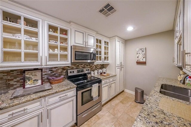 kitchen with light stone countertops, appliances with stainless steel finishes, tasteful backsplash, sink, and white cabinets