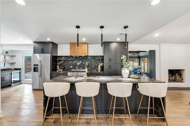 kitchen with dark stone counters, sink, hanging light fixtures, stainless steel fridge with ice dispenser, and beverage cooler