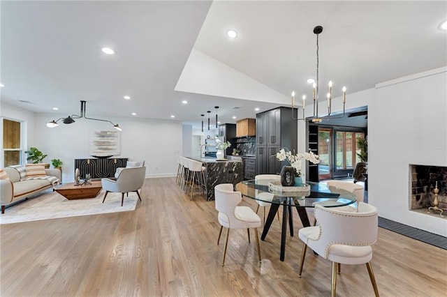 dining room featuring sink, a chandelier, lofted ceiling, and light wood-type flooring