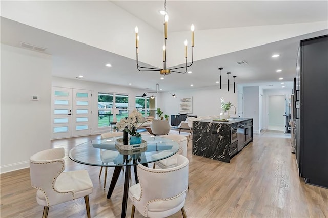 dining room with a chandelier, sink, light hardwood / wood-style floors, and vaulted ceiling