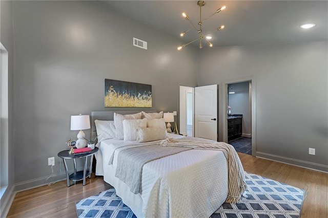 bedroom with dark hardwood / wood-style floors, a chandelier, high vaulted ceiling, and ensuite bath