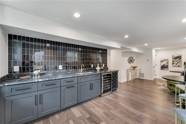 bar with tasteful backsplash, sink, dark stone counters, and beverage cooler