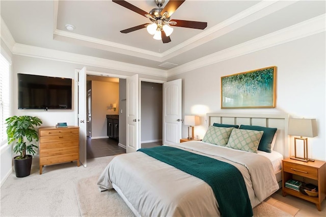 bedroom with ceiling fan, crown molding, ensuite bathroom, a tray ceiling, and carpet