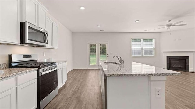 kitchen with sink, white cabinetry, light stone counters, stainless steel appliances, and a kitchen island with sink