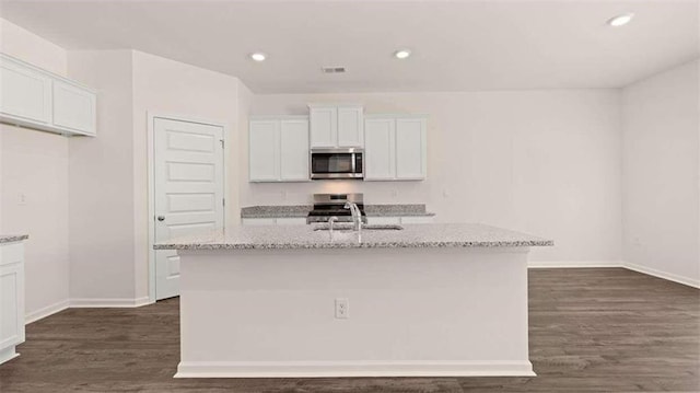 kitchen featuring stainless steel appliances, an island with sink, light stone countertops, and white cabinets