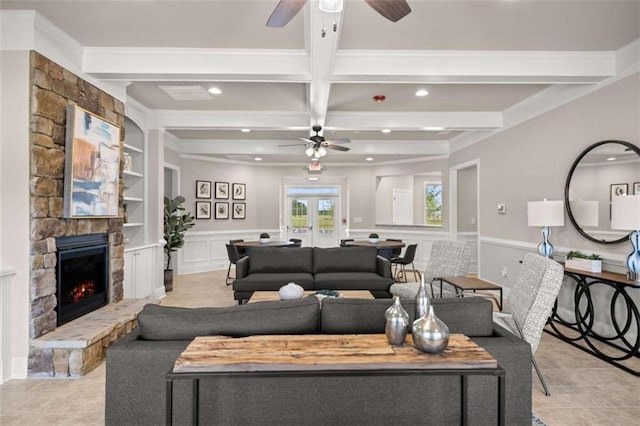 living room with ceiling fan, beam ceiling, built in shelves, a stone fireplace, and french doors