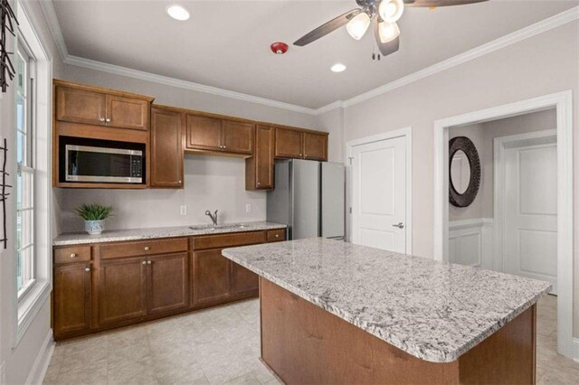 kitchen with a kitchen island, sink, ornamental molding, light stone counters, and stainless steel appliances