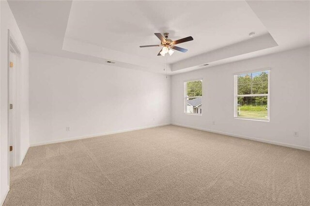 carpeted empty room featuring ceiling fan and a raised ceiling