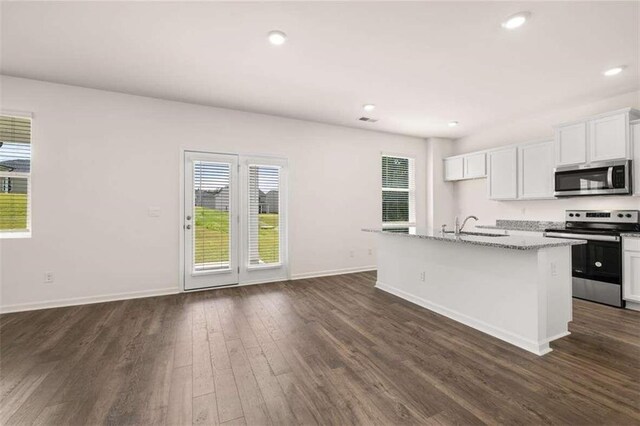 kitchen with a center island with sink, dark hardwood / wood-style floors, light stone countertops, appliances with stainless steel finishes, and white cabinetry