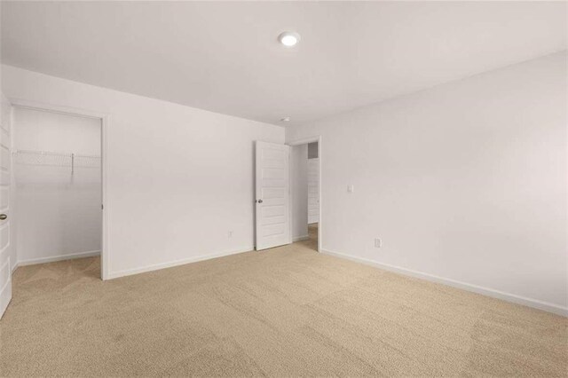 unfurnished bedroom featuring a spacious closet, light carpet, and a closet