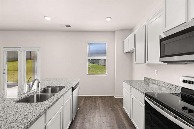 kitchen with light stone countertops, stainless steel appliances, dark wood-type flooring, sink, and white cabinets