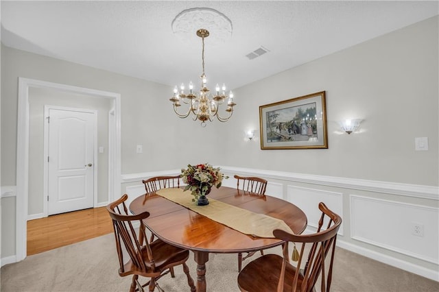 dining room with light carpet, a chandelier, a wainscoted wall, and a decorative wall