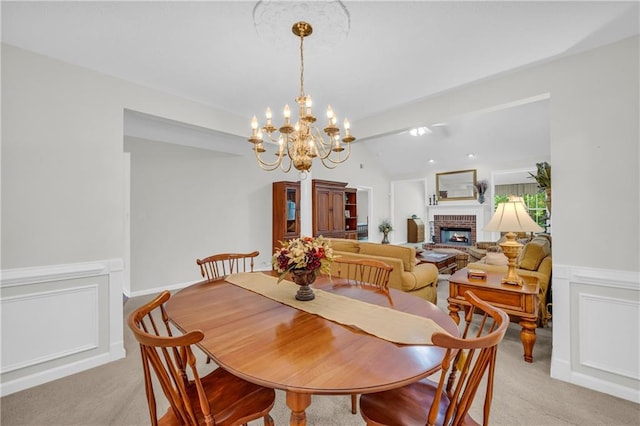 dining area featuring a brick fireplace, a chandelier, light carpet, wainscoting, and lofted ceiling