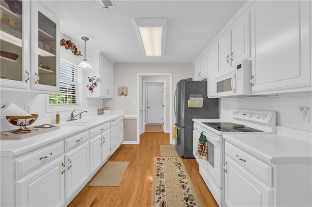 kitchen with white appliances, white cabinets, light wood-style floors, a sink, and decorative backsplash