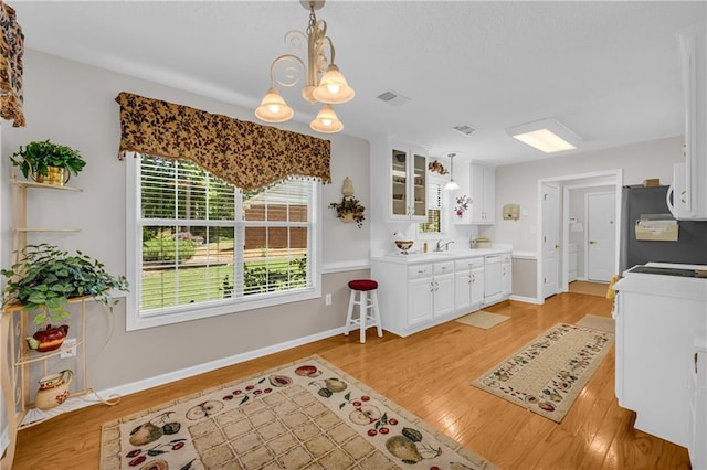 kitchen featuring a chandelier, freestanding refrigerator, white cabinets, light wood-style flooring, and glass insert cabinets