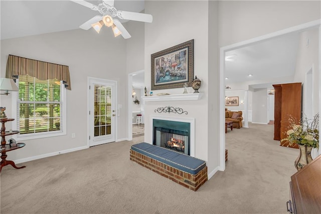 living room featuring carpet floors, high vaulted ceiling, a lit fireplace, baseboards, and a ceiling fan