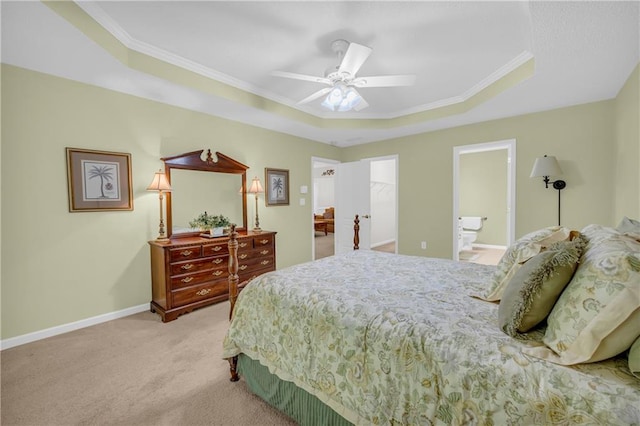 carpeted bedroom featuring a tray ceiling, crown molding, baseboards, ceiling fan, and ensuite bathroom