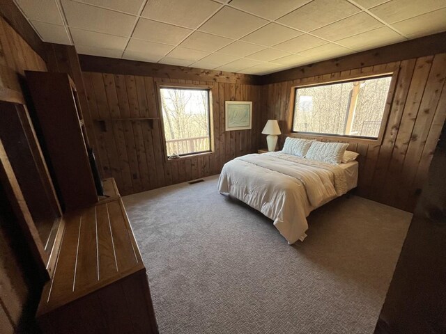 carpeted bedroom with visible vents and wooden walls