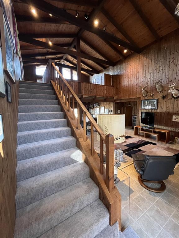 stairway with beam ceiling, wood walls, high vaulted ceiling, wooden ceiling, and tile patterned floors