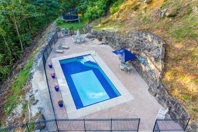 view of swimming pool featuring a trampoline and fence