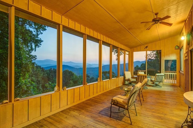 unfurnished sunroom featuring lofted ceiling, plenty of natural light, ceiling fan, and a mountain view