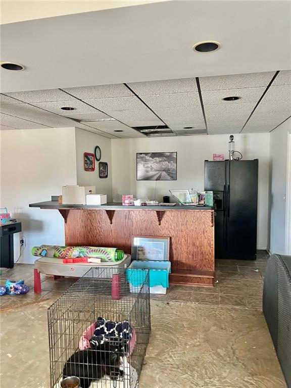 interior space featuring a drop ceiling, concrete floors, and black fridge