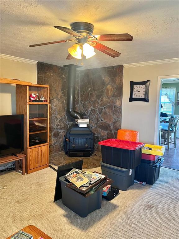 living room featuring carpet floors, ornamental molding, a wood stove, and a textured ceiling