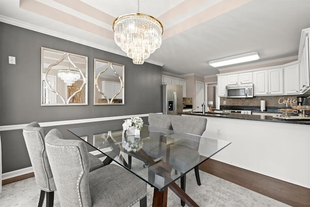 dining space with ornamental molding, a tray ceiling, a chandelier, and light hardwood / wood-style flooring