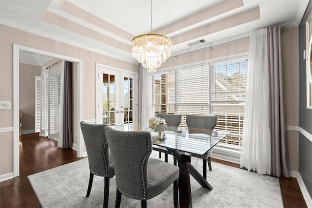 dining area with a raised ceiling, dark wood-type flooring, a chandelier, and french doors