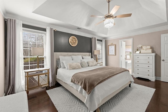 bedroom with dark wood-type flooring, ensuite bath, ornamental molding, and a tray ceiling