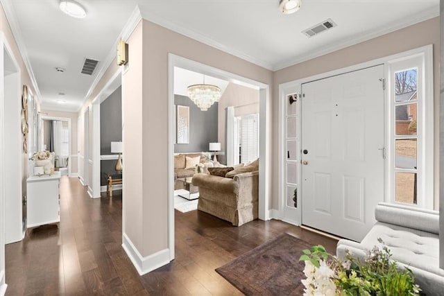 entryway with dark wood-type flooring, ornamental molding, and an inviting chandelier