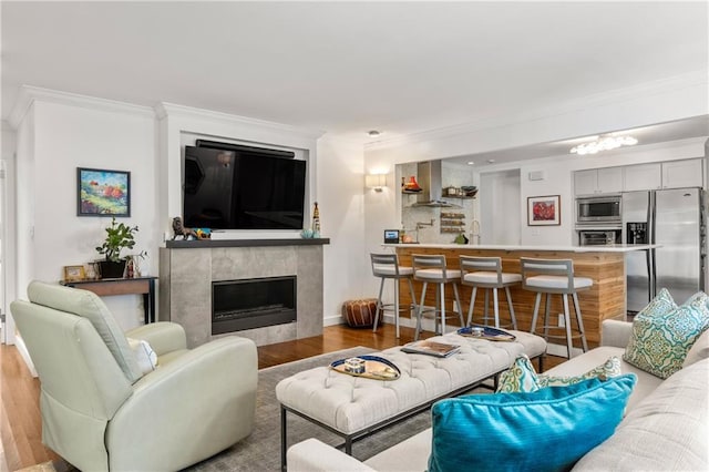 living room featuring a fireplace, light hardwood / wood-style flooring, ornamental molding, and sink