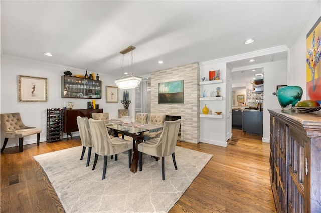 dining room featuring built in shelves, a fireplace, ornamental molding, and hardwood / wood-style flooring