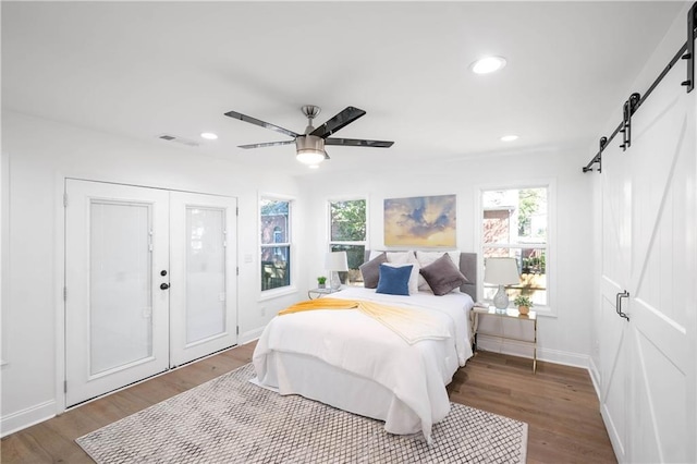 bedroom with ceiling fan, a barn door, multiple windows, and hardwood / wood-style flooring