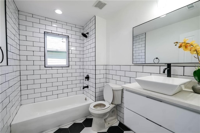 full bathroom with toilet, tiled shower / bath combo, tile patterned flooring, tile walls, and vanity