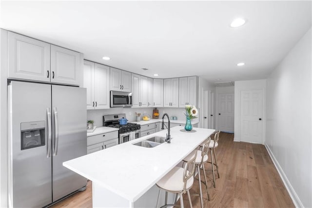 kitchen with sink, light hardwood / wood-style flooring, a kitchen island with sink, appliances with stainless steel finishes, and a kitchen breakfast bar