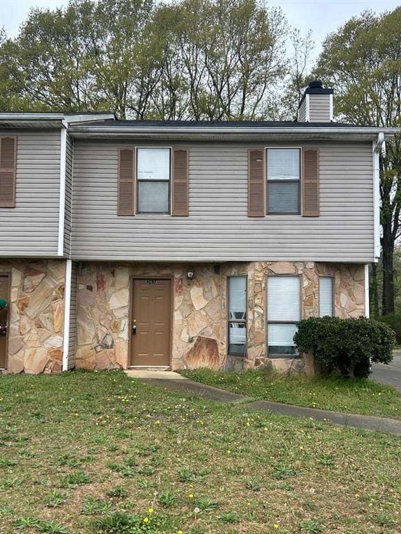 townhome / multi-family property with a chimney, a front yard, and stone siding