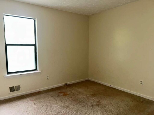 unfurnished room featuring carpet flooring, visible vents, baseboards, and a textured ceiling