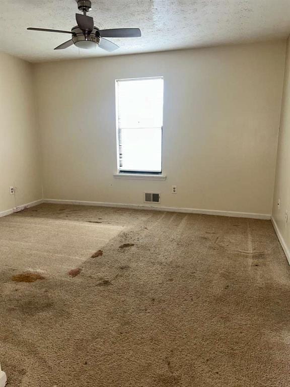 empty room with baseboards, carpet flooring, a textured ceiling, visible vents, and ceiling fan