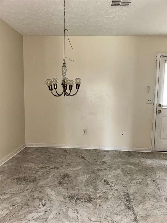 unfurnished dining area with a chandelier, a textured ceiling, baseboards, and visible vents